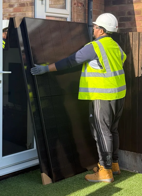 ECONEXIS installer in a hard hat and hi-vis carrying a solar panel on install day in Bedford