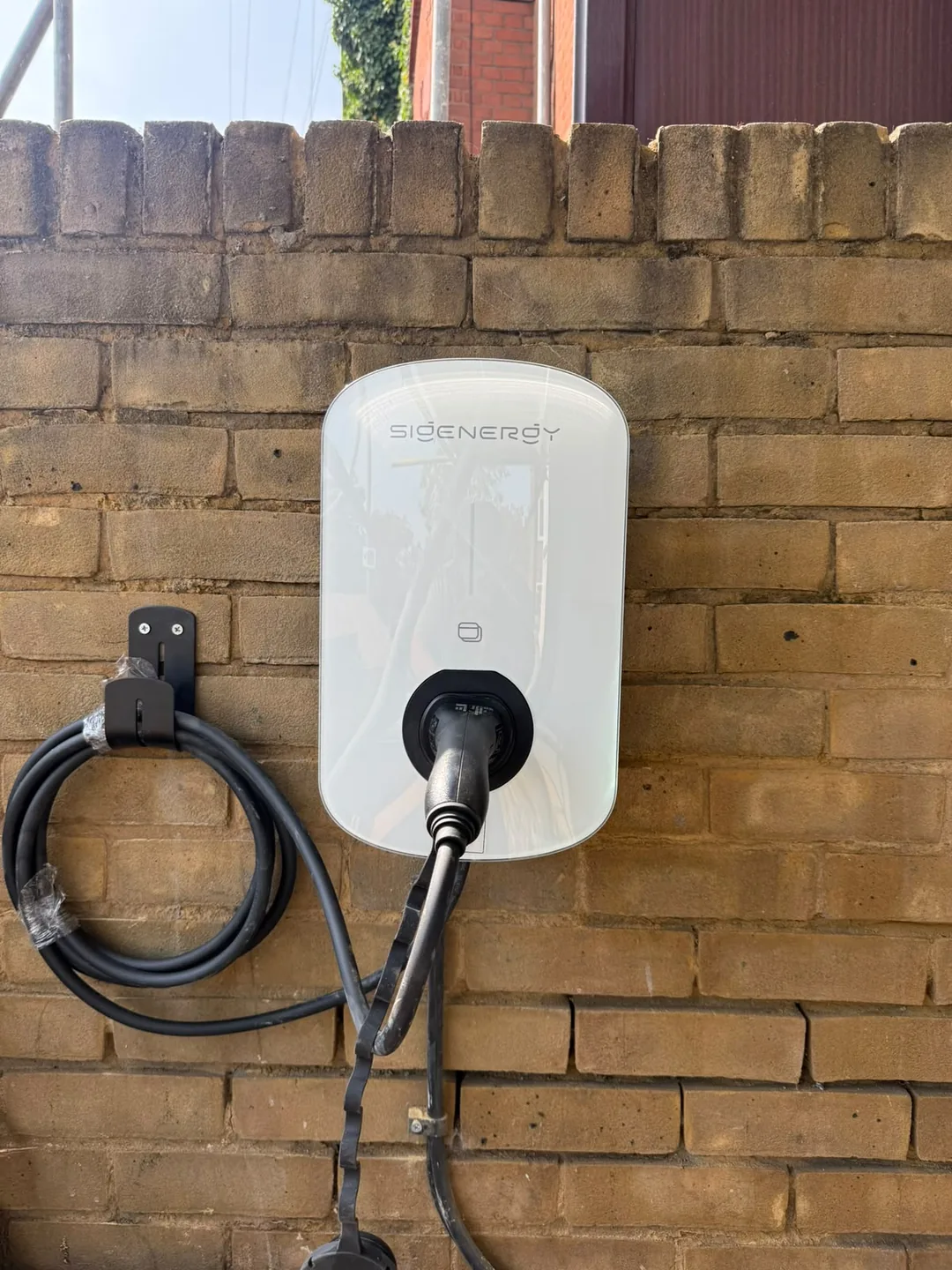 Sigenergy EV charger fitted on an outside brick wall by ECONEXIS, with the charging cable on its own wall holder